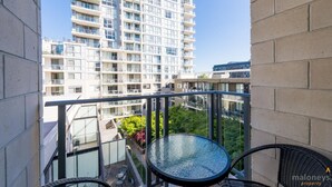 A balcony with a glass table and chairs, overlooking a high-rise building and greenery.