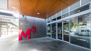 A modern building entrance with a large 'M3' sign, glass doors, and a 'KAMI' restaurant in the background. - Accommodate Canberra - Mode (Braddon)