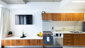 A modern kitchen with wooden cabinets, a built-in oven, a stainless steel sink, and a flat-screen TV mounted on the wall. - Accommodate Canberra - Mode (Braddon)