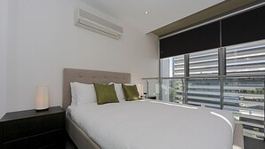 A modern hotel room with a large bed, a nightstand, a lamp, and a window with a view of the city. - Accommodate Canberra - Mode (Braddon)