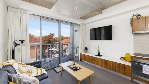 A modern living room with a sofa, a coffee table, and a sliding glass door leading to a balcony. - Accommodate Canberra - Mode (Braddon)