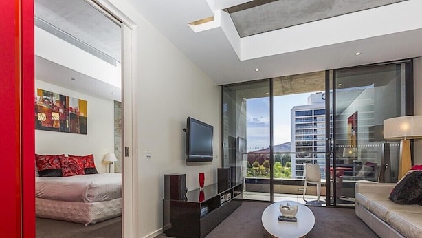 Una sala de estar moderna con un sofá, una mesa de centro, un televisor y un balcón con vistas a edificios y zonas verdes.
