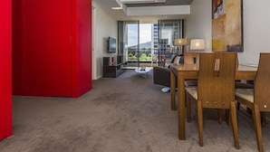 Una habitación de hotel moderna con zona de comedor, televisión y un amplio ventanal con vistas al exterior.