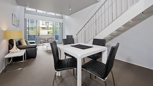 Un interior moderno con una mesa de comedor blanca, sillas negras, un sofá y una escalera.