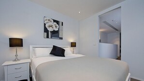 Una habitación de hotel moderna con una cama grande, dos mesitas de noche con lámparas, un espejo amplio y una obra de arte floral en la pared.