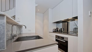 Una cocina moderna con muebles blancos, un lavamanos de acero inoxidable y un horno empotrado.