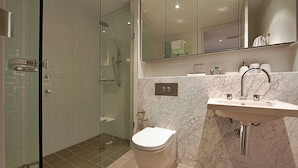 Un baño moderno con ducha acristalada, inodoro blanco y lavabo de mármol.