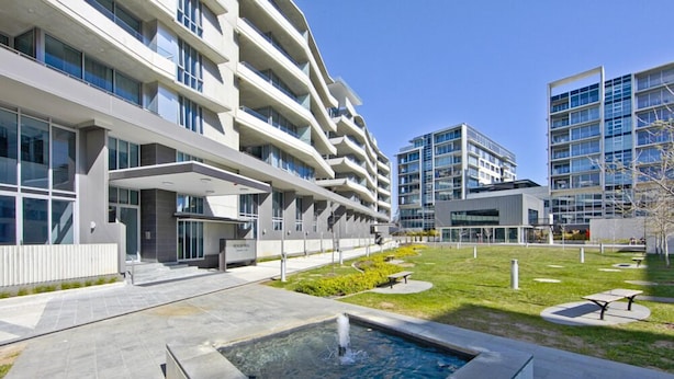 Un hotel moderno con varios pisos, zonas de estar al aire libre y una fuente central.
