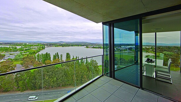 A modern balcony with a glass door, offering a view of a river, greenery, and distant hills. - Accommodate Canberra - The ApARTments (Canberra)