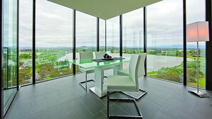 A modern meeting room with a glass table, white chairs, and a view of a river and landscape. - Accommodate Canberra - The ApARTments (Canberra)