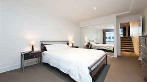 A modern hotel room with a large bed, bedside tables with lamps, a dresser, and a mirror reflecting the room.