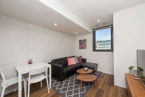 A compact living space with a black leather sofa, a white dining table, and a small round coffee table.