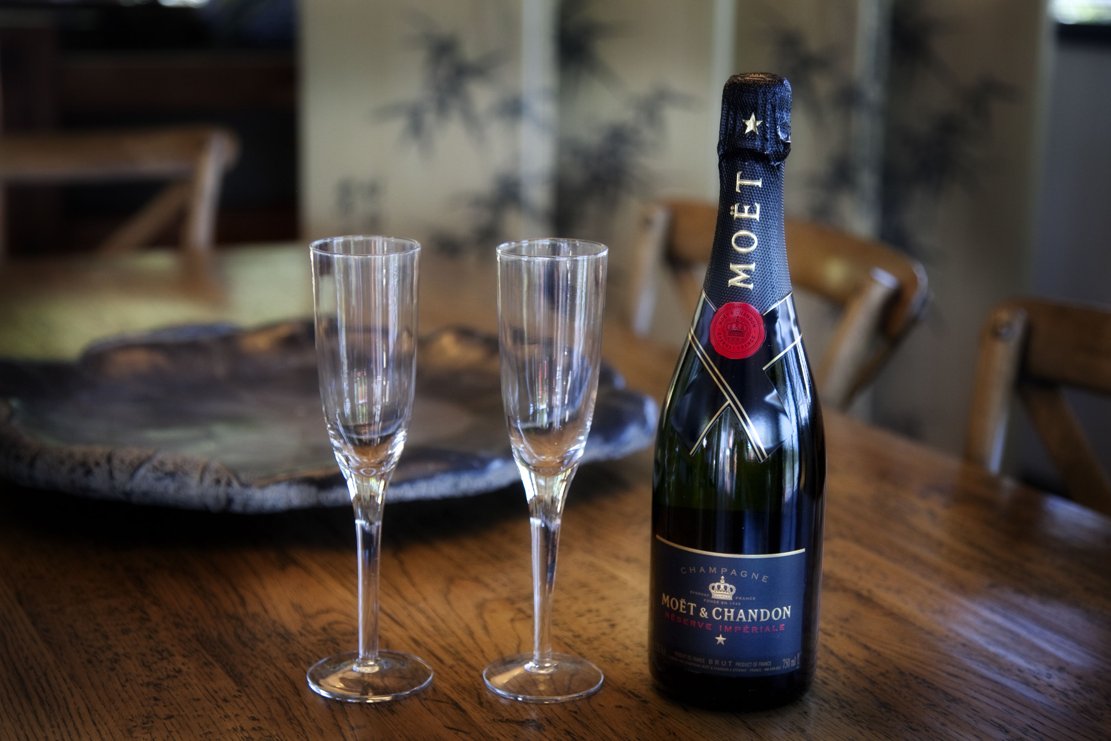 A bottle of Moët & Chandon champagne and two empty glasses on a wooden table.