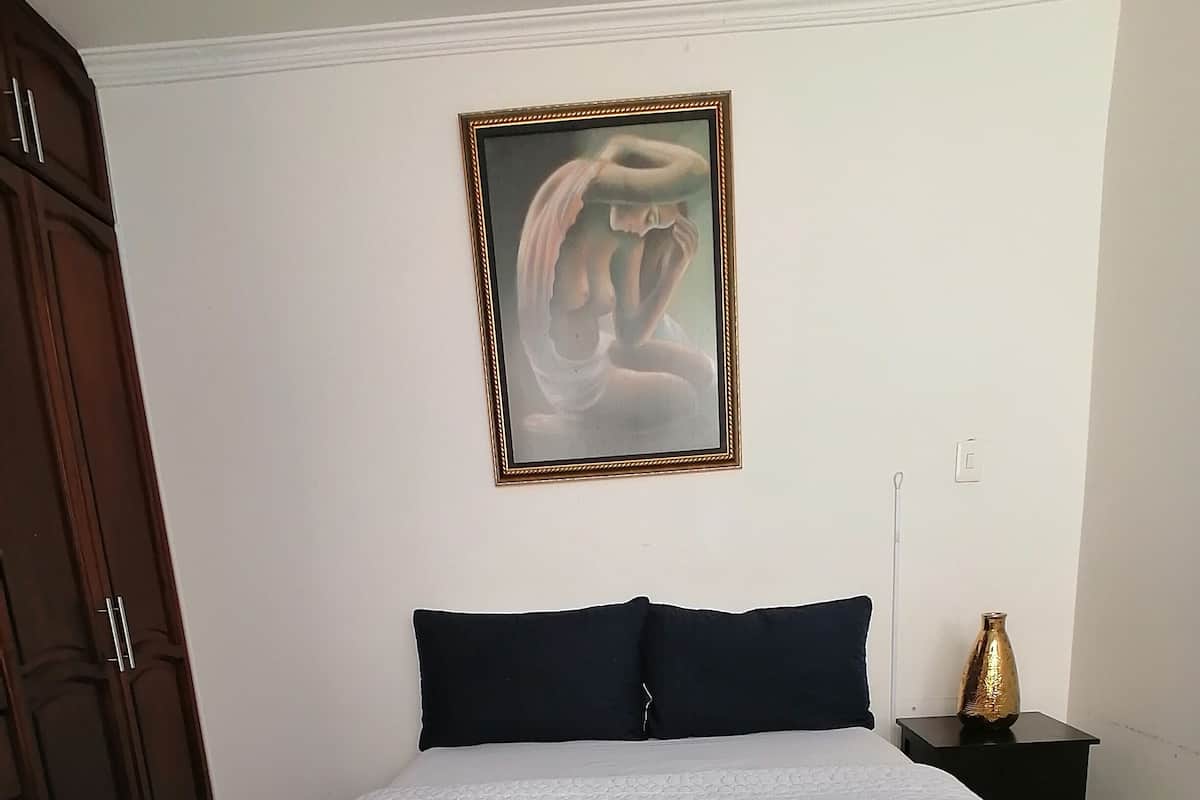 A neatly made bed with a white quilt, a dark headboard, and a framed artwork on the wall.