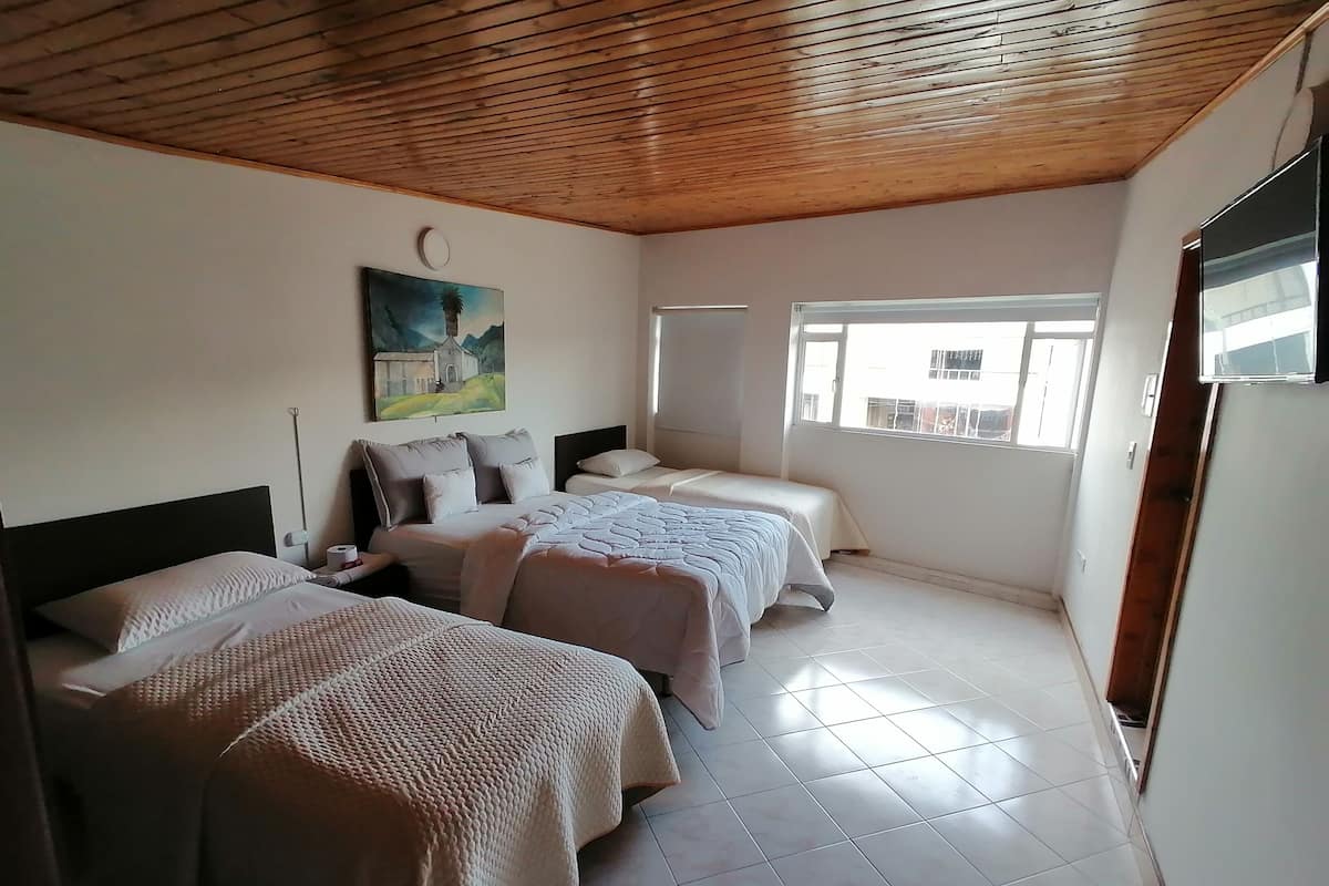 A hotel room with two beds, a painting on the wall, a window, and a ceiling with wooden beams.