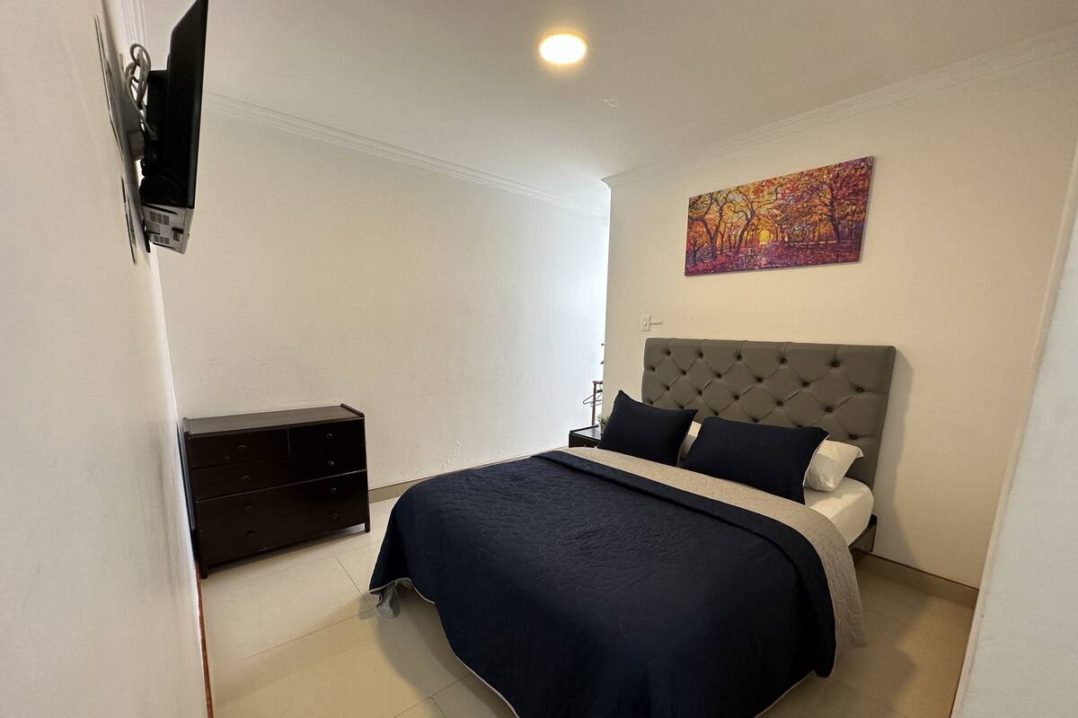 A bedroom with a bed, a nightstand, a dresser, and a painting on the wall.