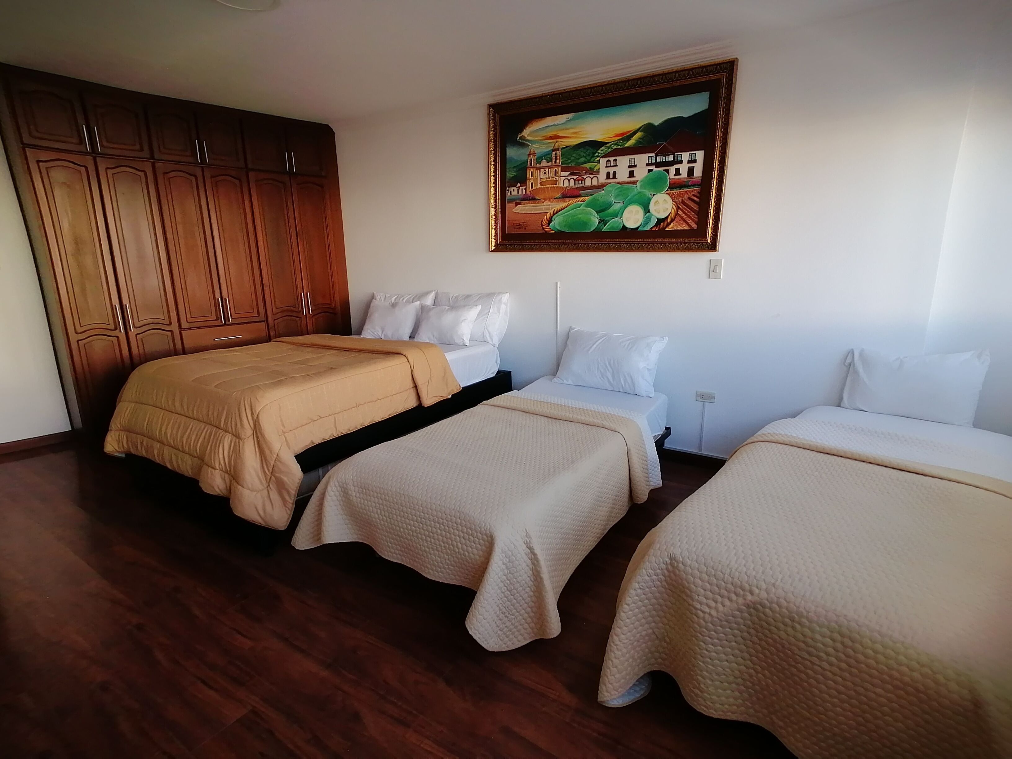 A hotel room with two beds, wooden wardrobe, and a painting on the wall.