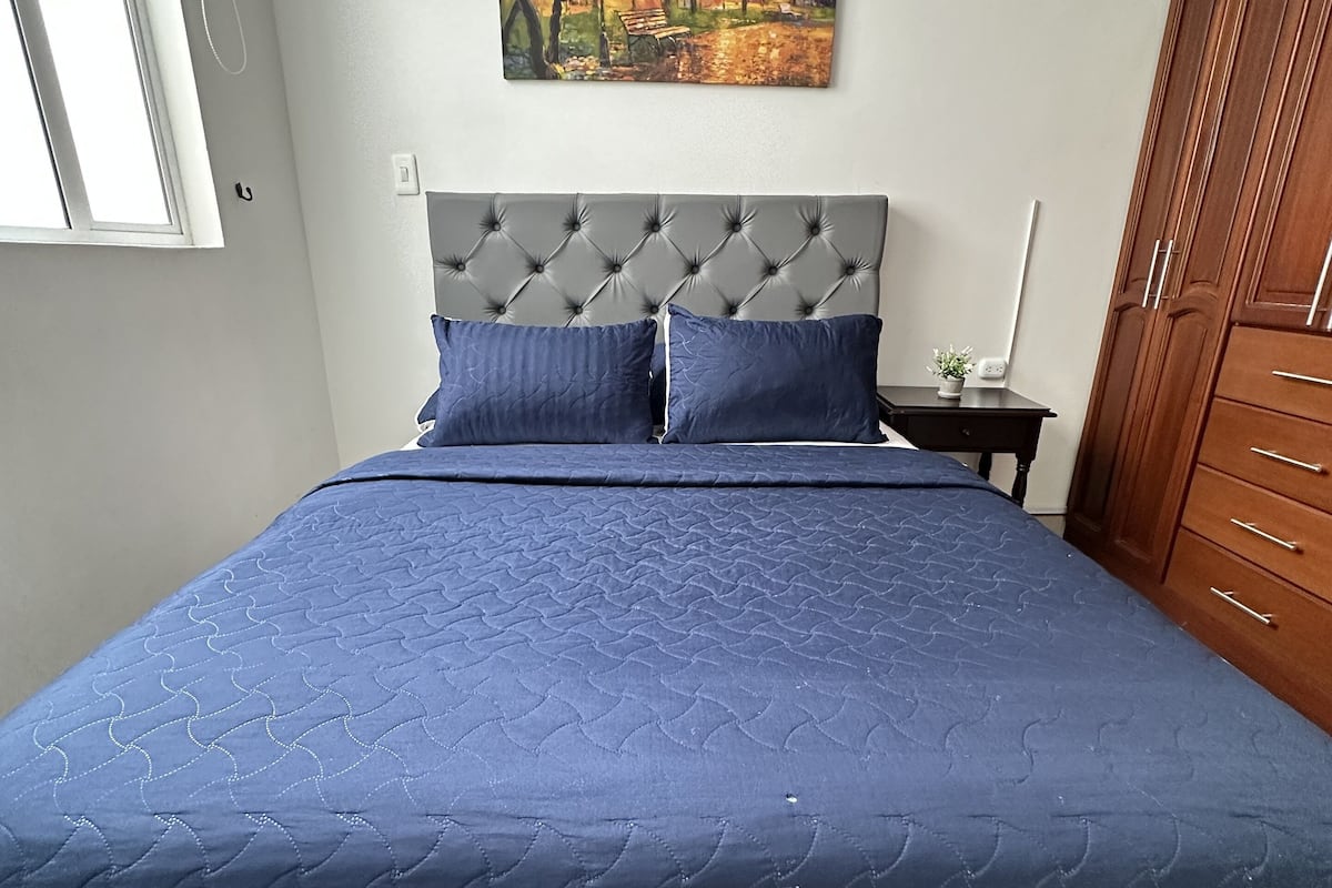 A bedroom with a bed, a nightstand, a painting, and a wardrobe.