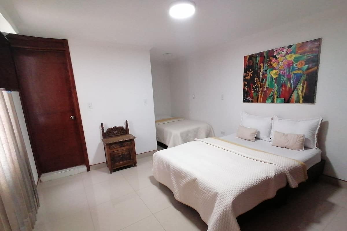 A hotel room with two beds, a wooden nightstand, a painting on the wall, and a door.