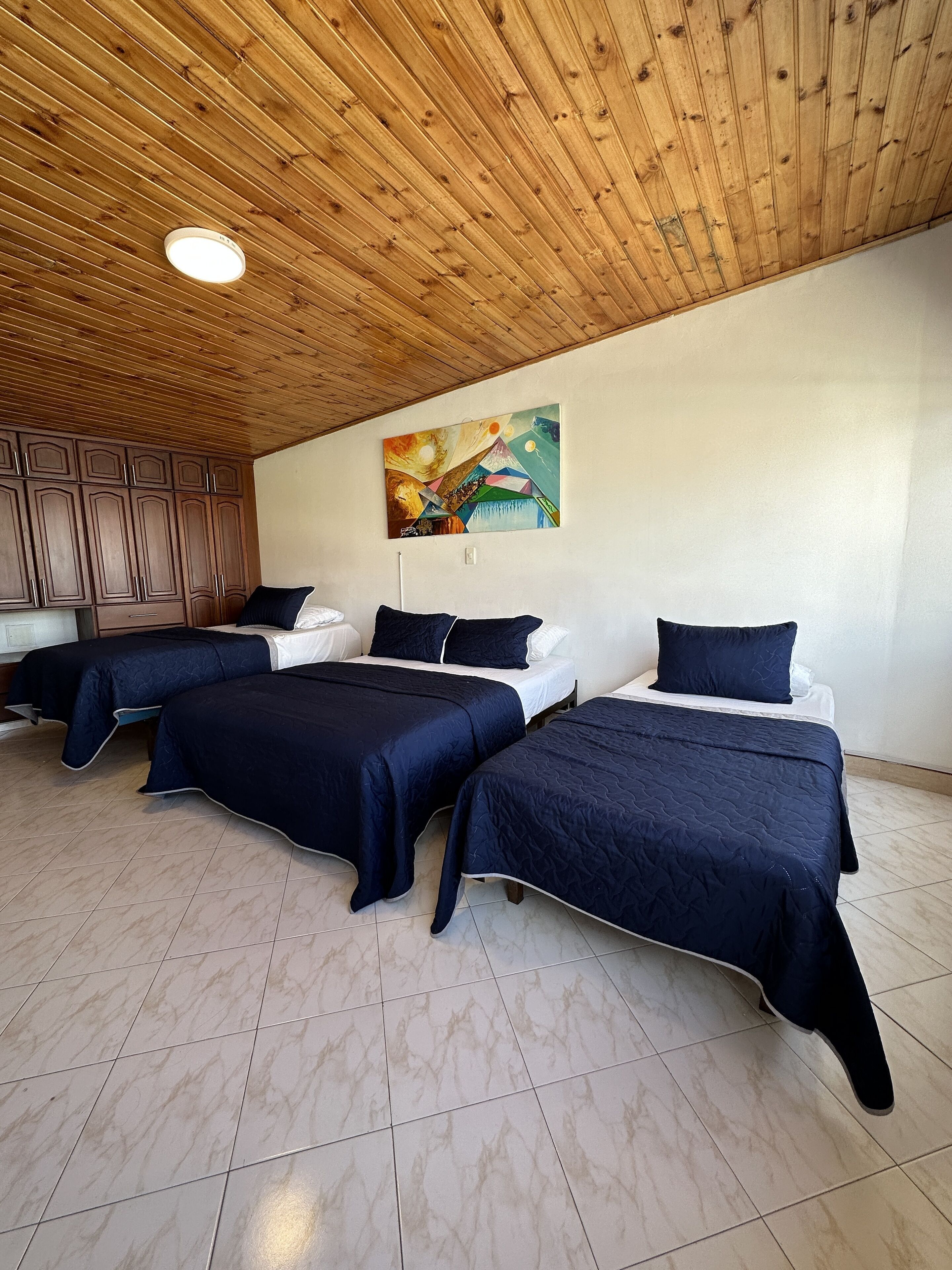 A room with three beds, wooden ceiling, and a painting on the wall.