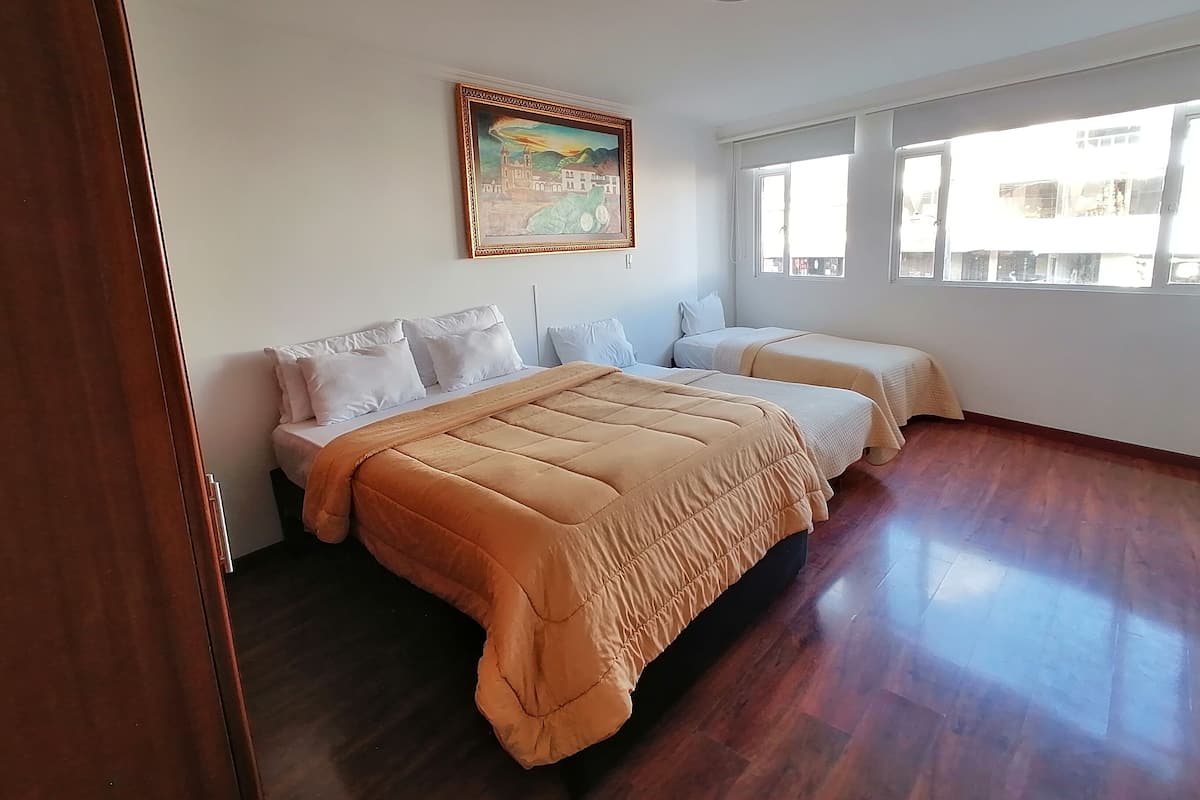 A hotel room with a large bed, two smaller beds, a painting on the wall, and large windows.