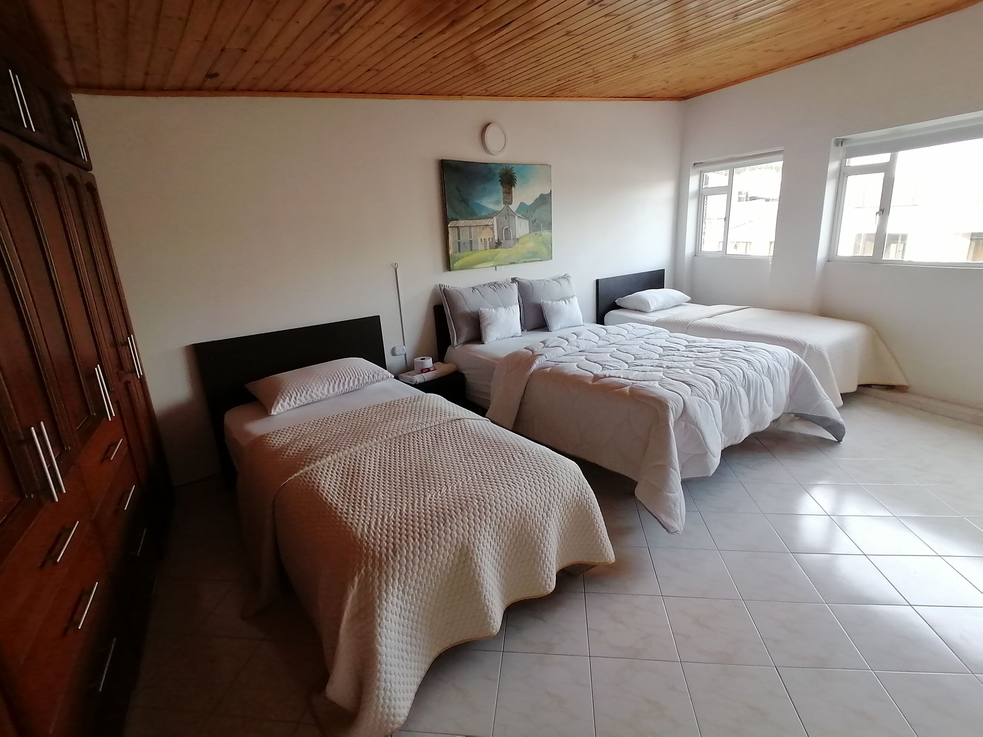 A bedroom with two beds, wooden ceiling, white walls, and a painting.
