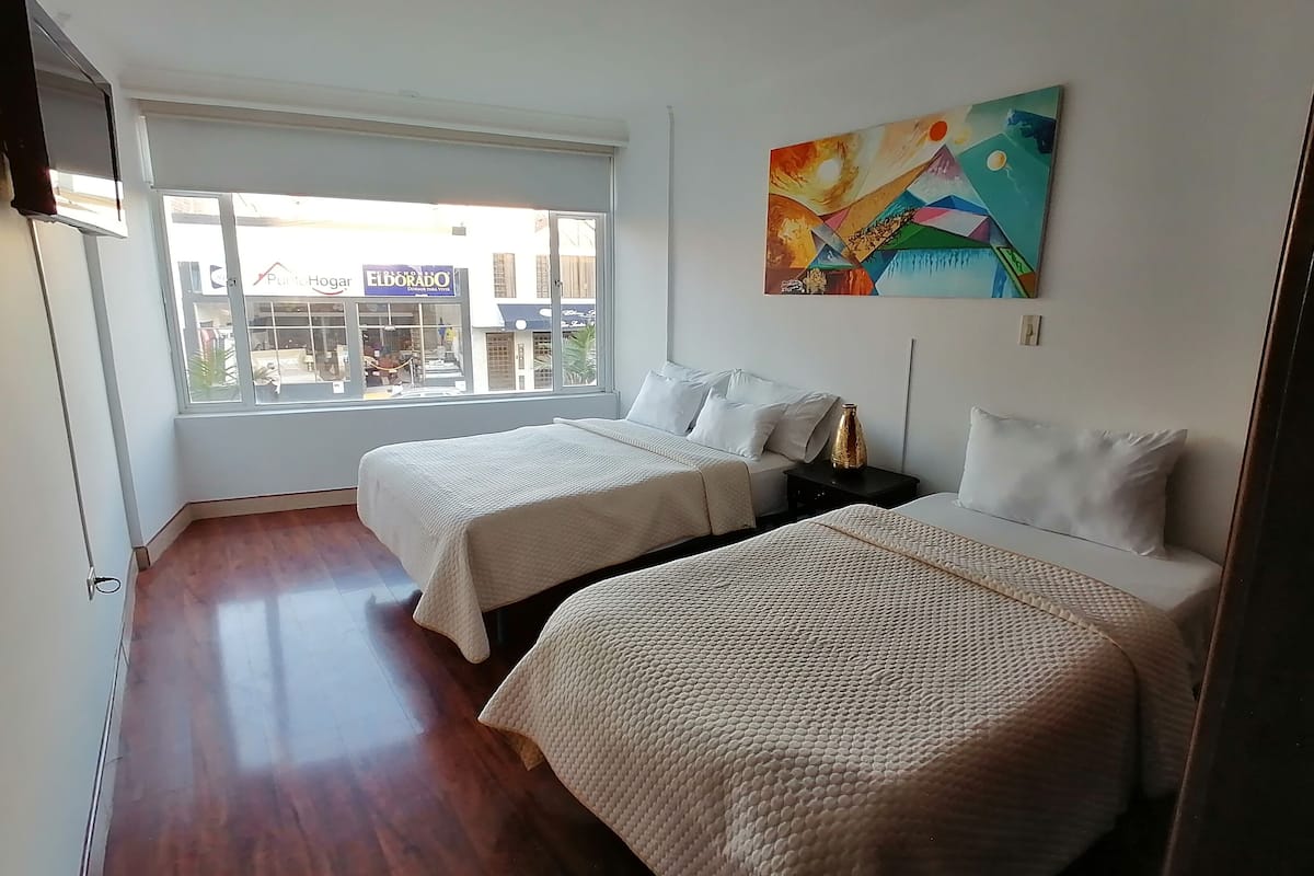 A hotel room with two beds, a large window, and a colorful painting on the wall.