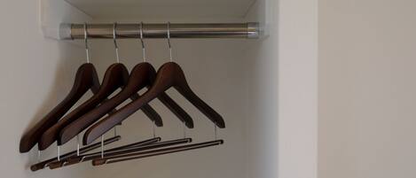 A closet with a white shelf and a metal rod holding wooden hangers and a metal hanger.