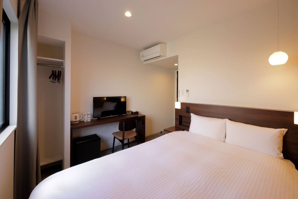 A hotel room with a large bed, a desk with a flat-screen TV, a chair, and a wardrobe.