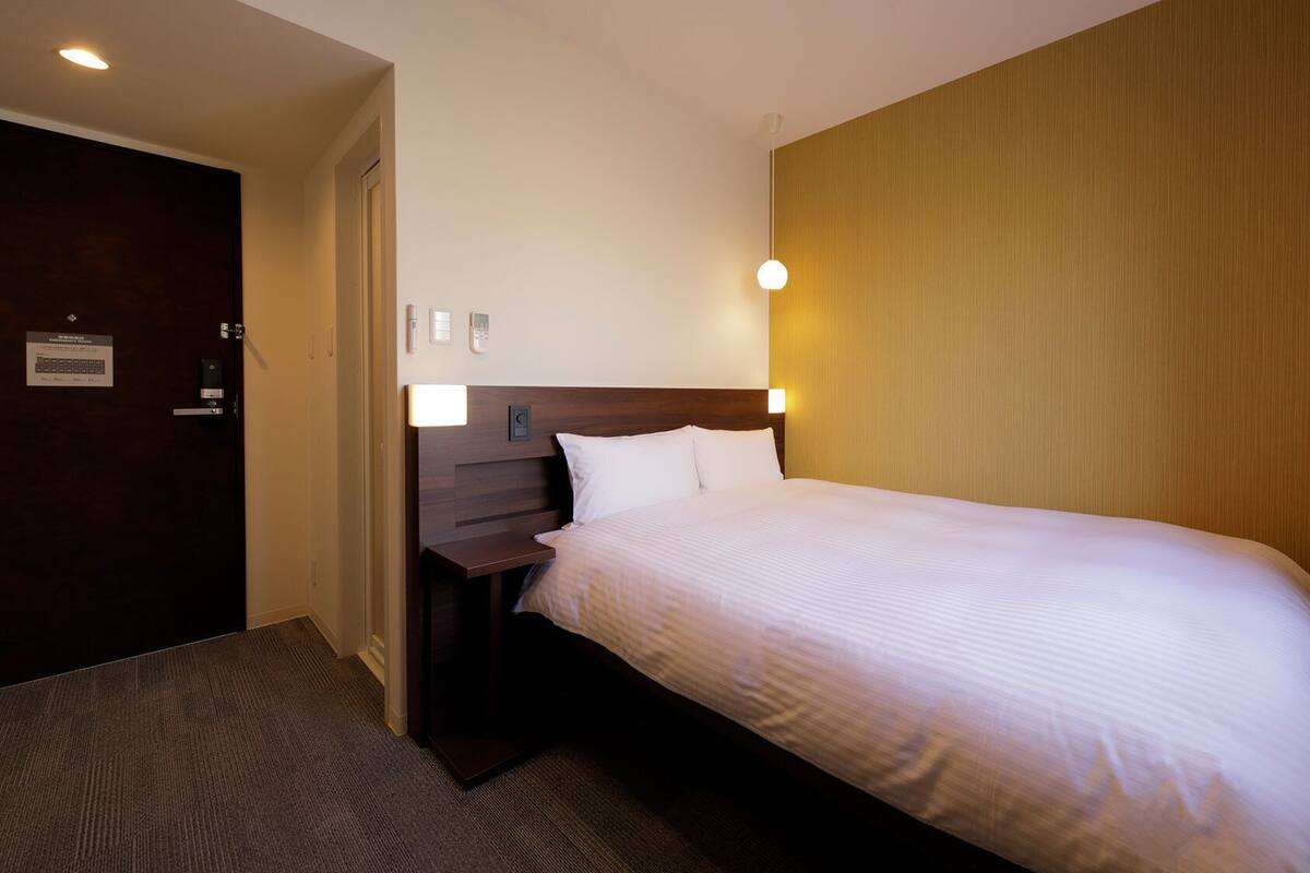 A hotel room with a bed, bedside table, lamp, and a door with a sign.