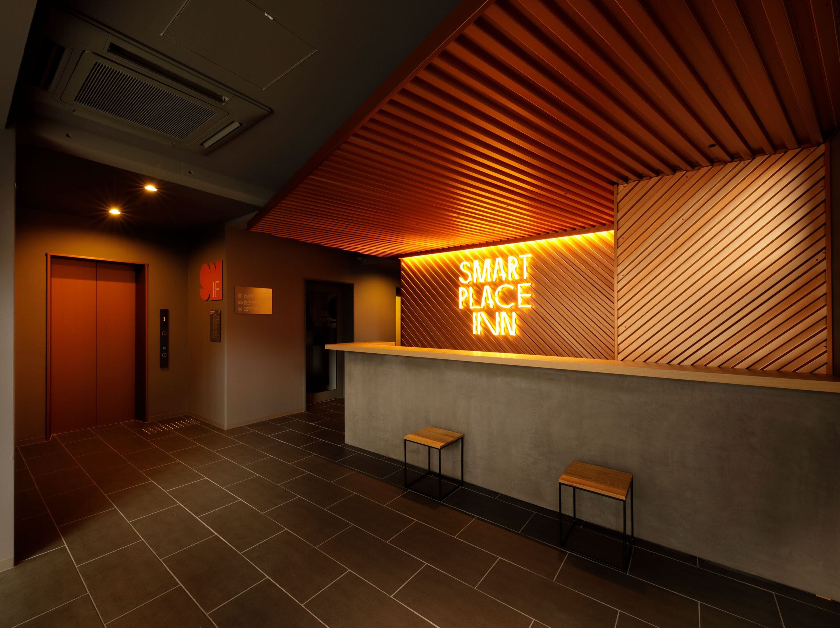 A reception area with a wooden slatted ceiling, a reception desk, two stools, and a sign that reads "SMART PLACE INN".