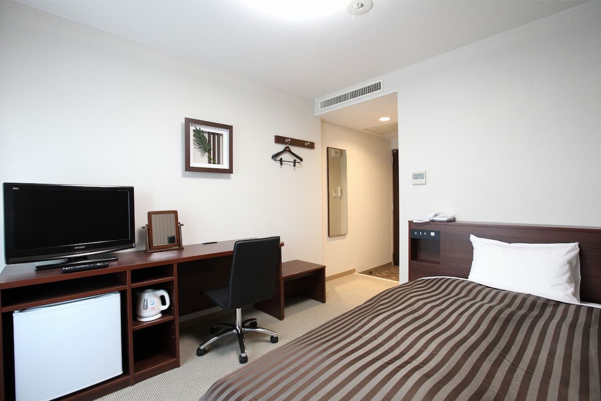 Quarto de hotel com cama, escrivaninha com televisão, cafeteira e espelho.