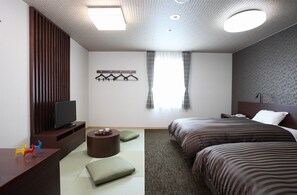 Ett modernt hotellrum med en platt-TV, två sängar, en liten sittgrupp och ett fönster med gardiner.