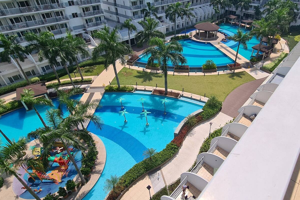 Un hotel de varios niveles con un área de piscina central, múltiples balcones y una zona de estar cubierta.