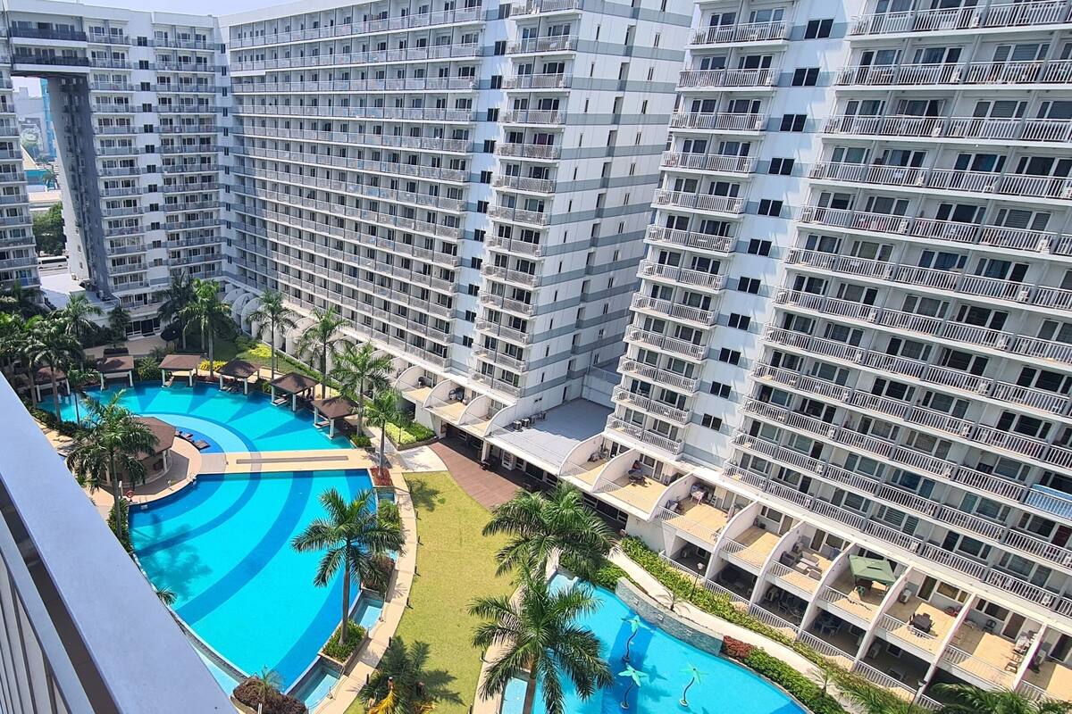 Un hotel de gran altura con múltiples balcones, una piscina central y palmeras.
