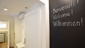 A hallway with a white door, a blackboard with 'Welcome!' written in multiple languages, and a radiator on the wall. - B&B Isola Memmia (Padova)