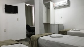 Quarto de hotel com duas camas, uma escrivaninha com cadeira, televisão e ar condicionado.