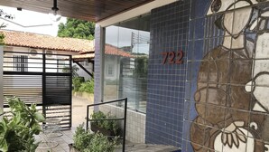 Entrada de prédio com parede revestida de azulejos, placa com o número '722' e escada que leva a uma área coberta.