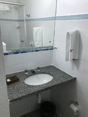 Un baño con lavamanos de encimera de granito, un espejo, un perchero para toallas y un cubo de basura.