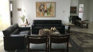Uma sala de estar com um sofá preto, duas poltronas, uma mesa de centro e um quadro na parede.
