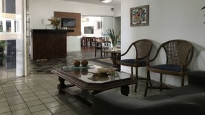 Uma área de recepção moderna com uma mesa de vidro, duas cadeiras de vime, um sofá e uma área de refeições ao fundo.