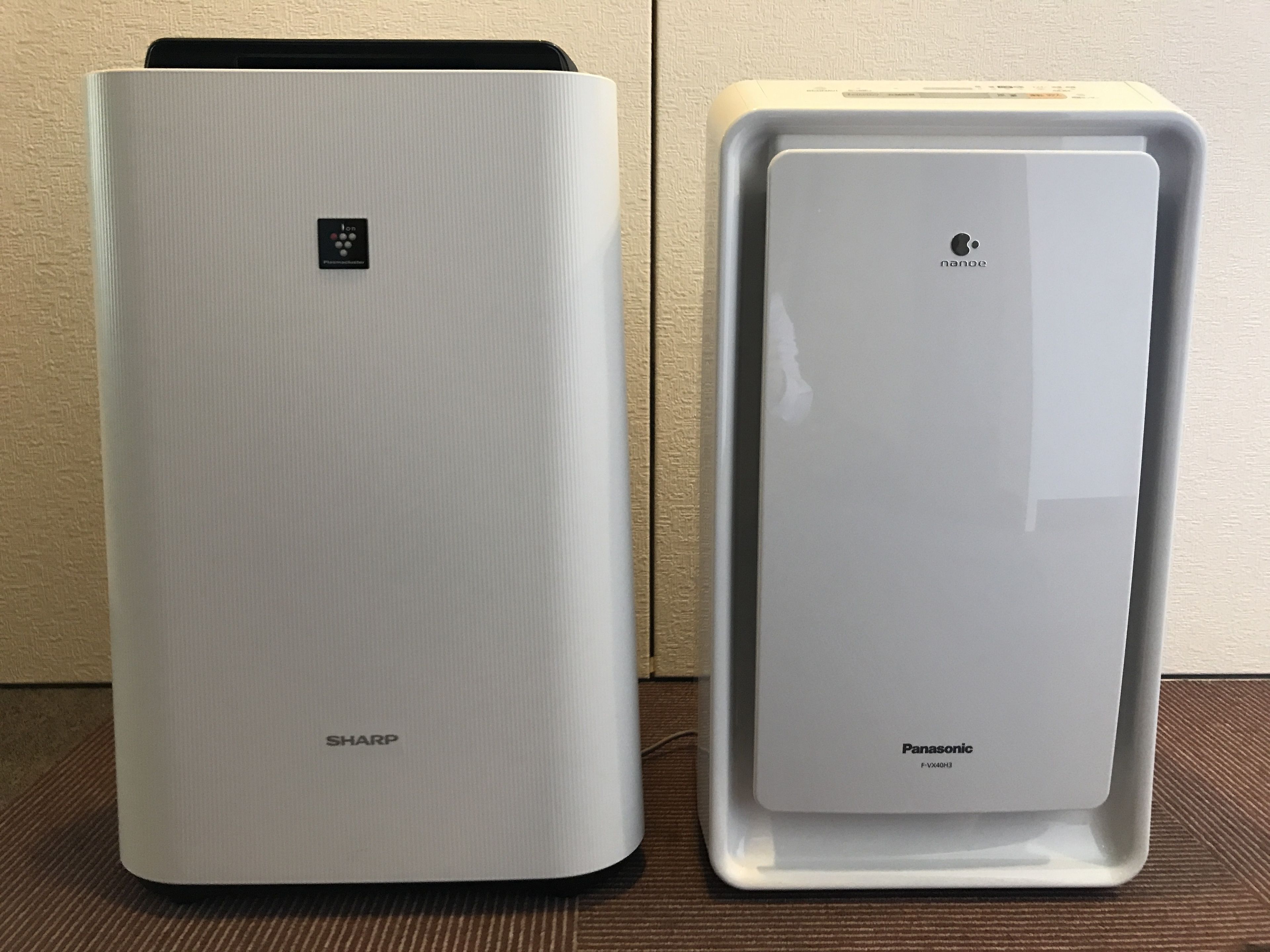 Dos unidades de aire acondicionado blancas, una con la etiqueta 'SHARP' y la otra 'Panasonic', sobre una superficie marrón frente a una pared con textura.