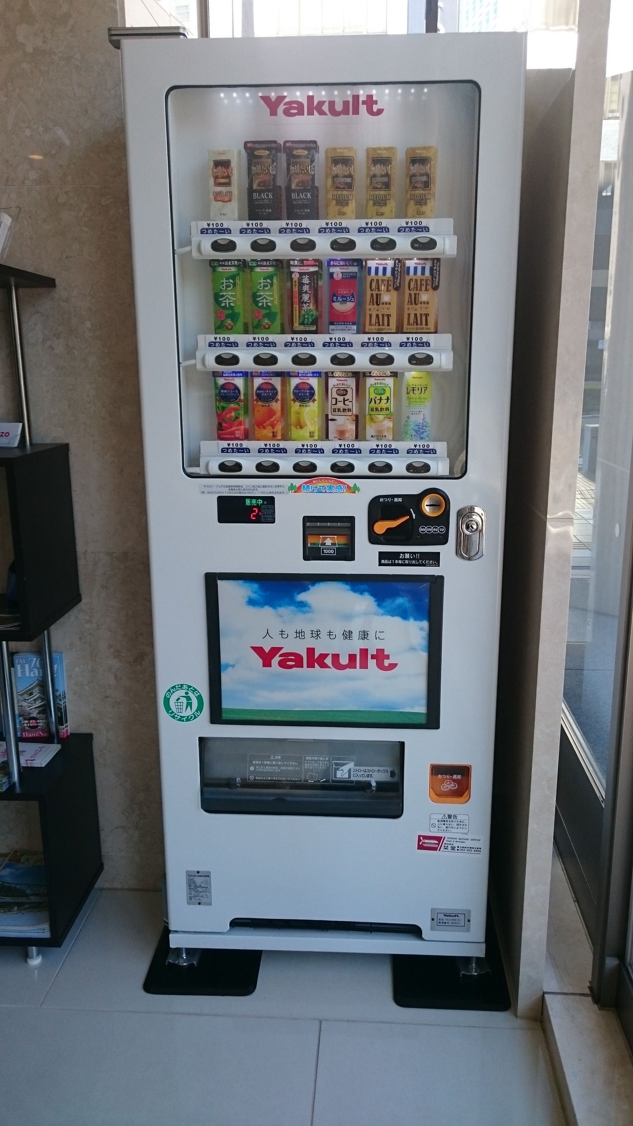 A vending machine with various drinks and snacks, including Yakult, coffee, and tea.