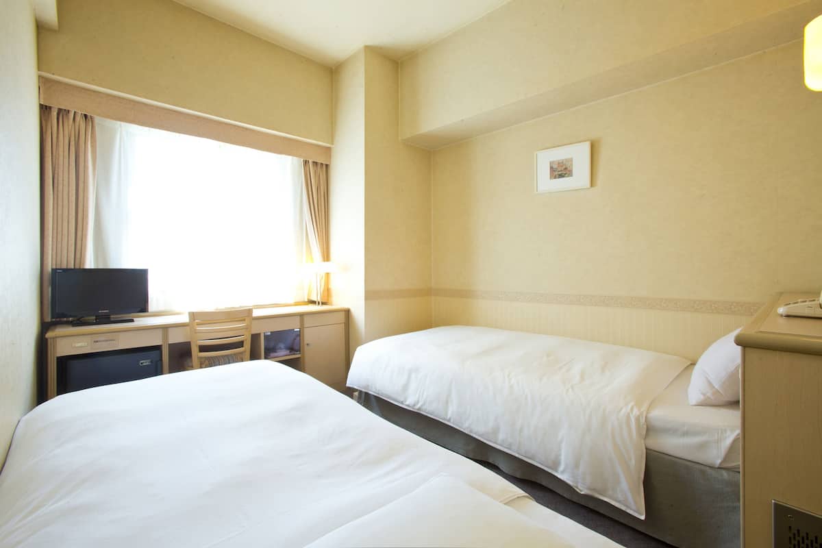 Una camera d'albergo con due letti, una scrivania con televisore e un mobiletto.