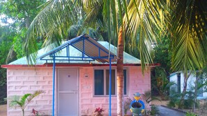 A pink building with a blue roof, a door, and windows. There are plants and a small statue in front.