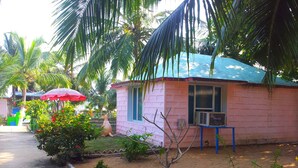 A pink building with a window and a sign, surrounded by palm trees and a red umbrella.