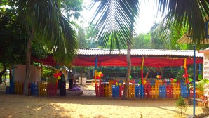 A sandy outdoor area with a colorful fence, a red canopy, and a small tree.