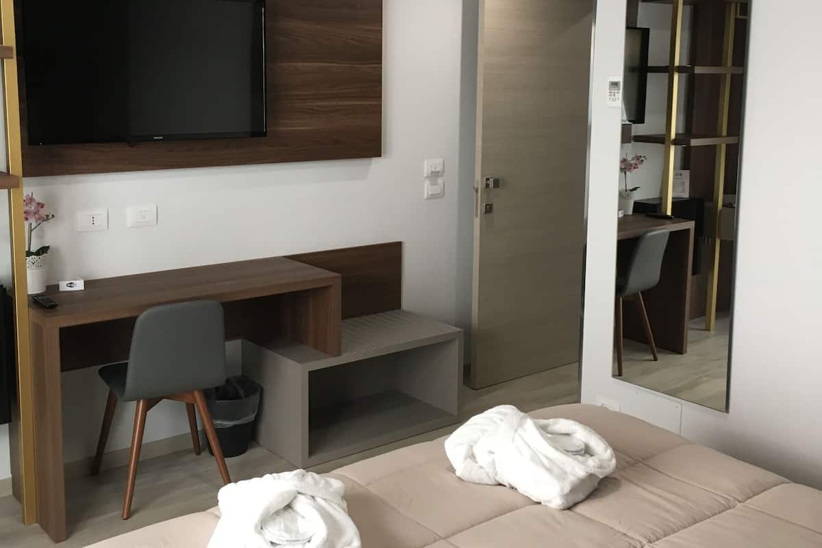 Una habitación de hotel moderna con una cama, un escritorio, una silla, un televisor y un espejo.