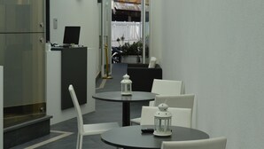 A modern hotel lobby with a reception desk, a round table with chairs, and a view of the outdoor area through a glass door. - 8 Room Hotel (Catania)