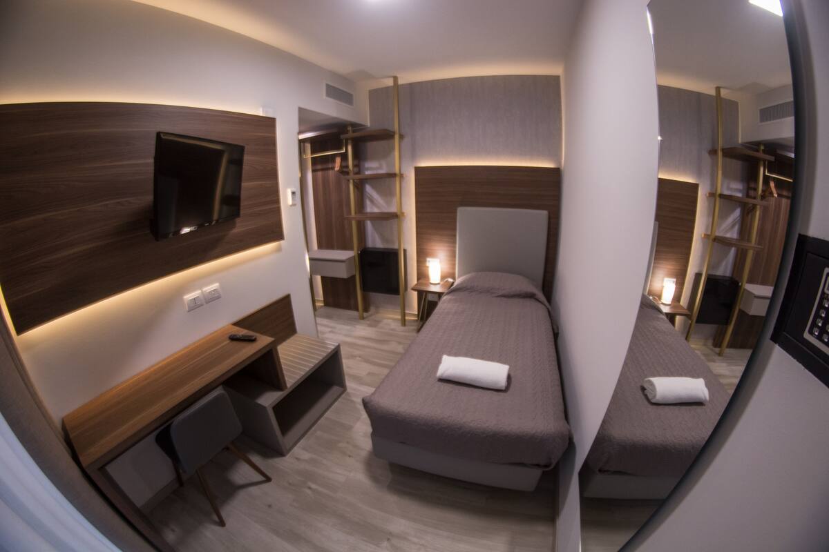 Habitación de hotel compacta con escritorio, dos camas individuales, una silla y un televisor.